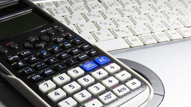 ノートPCのキーボード上に関数電卓が置かれている写真。統計の授業や学生指導のイメージ